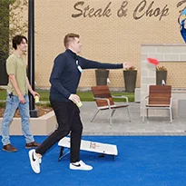 Person playing bean bag toss at District 121 in courtyard